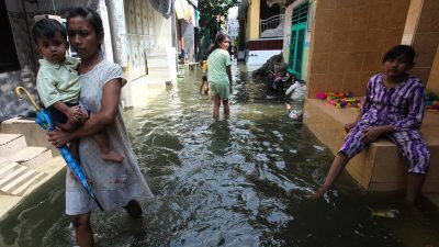 Warga berjalan melintasi banjir rob yang menggenangi kampung Kalianak Timur, Surabaya, Jawa Timur, Rabu (5/7/2023).